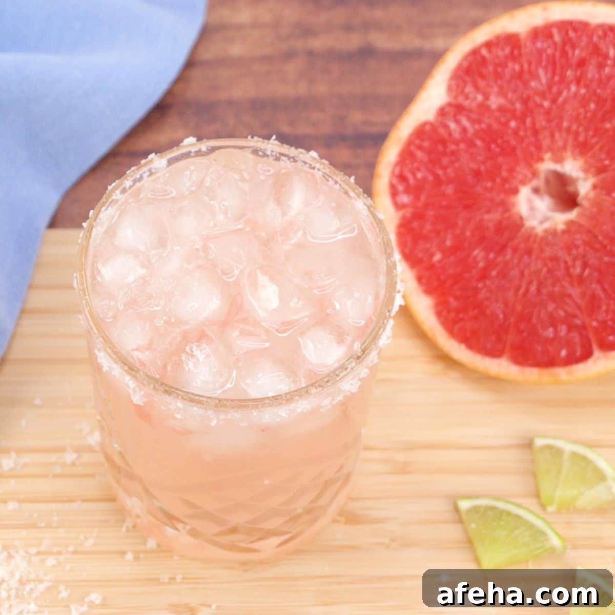 Quarter view of an easy Paloma cocktail in a salt rimmed lowball glass filled with ice. Hostess At Heart