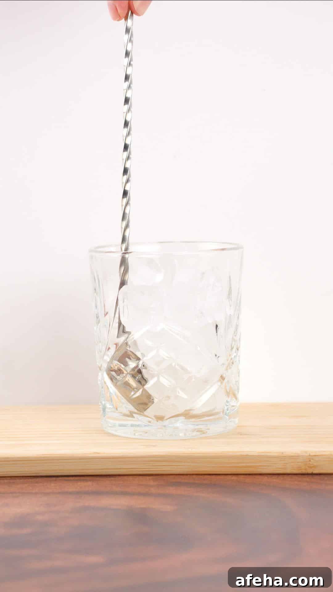 Chilling a cocktail glass by stirring ice into it.