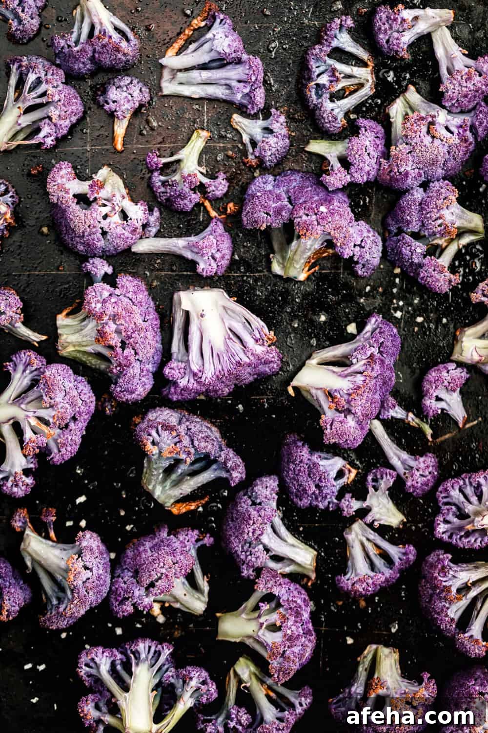 Purple Cauliflower Varieties: Flavor, Nutrition & Cooking Tips 9 roasted purple cauliflower florets, on a black baking sheet, overhead