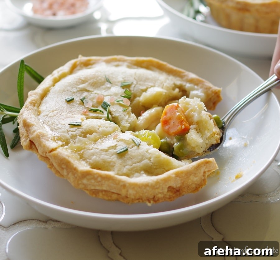Gluten-Free Chicken Pot Pie Recipe: Flaky Crust & Creamy Filling 4 a Gluten-Free Chicken Pot Pie topped with salt and rosemary on a white plate, with a spoon taking a bite out