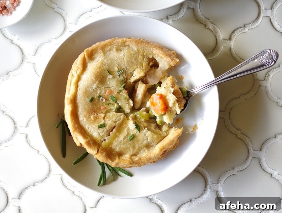 Gluten-Free Chicken Pot Pie Recipe: Flaky Crust & Creamy Filling 6 a top down view of a Gluten-Free Chicken Pot Pie topped with salt and rosemary on a white plate, with a spoon taking a bite out