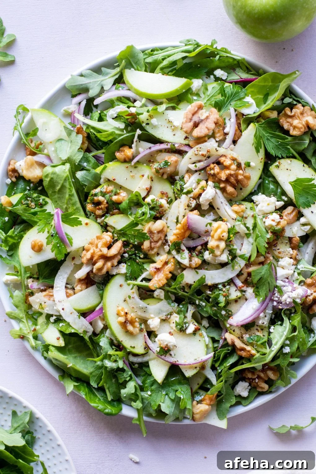 Large green salad on a round plate and a light colored background. Salad greens layered with thinly sliced green onion, thinly shaved fresh fennel, sliced red onion, walnuts, and torn parsley leaves. Drizzled with a mustardy dressing.