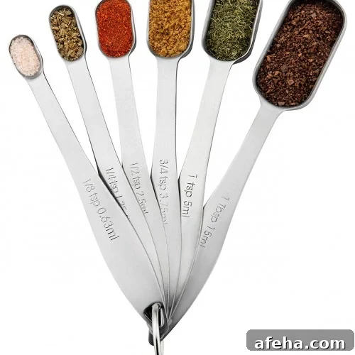 A set of six metal measuring spoons, each filled with a different spice or herb, fanned out in a semi-circle and connected by a metal ring.
