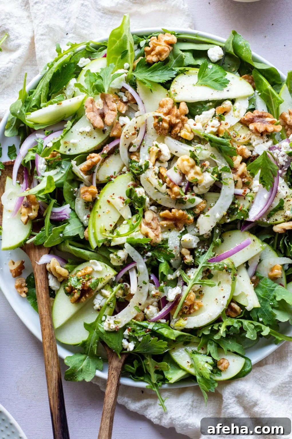 Large green salad on a round plate and a light colored background. Salad greens layered with thinly sliced green onion, thinly shaved fresh fennel, sliced red onion, walnuts, and torn parsley leaves. Drizzled with a mustardy dressing.