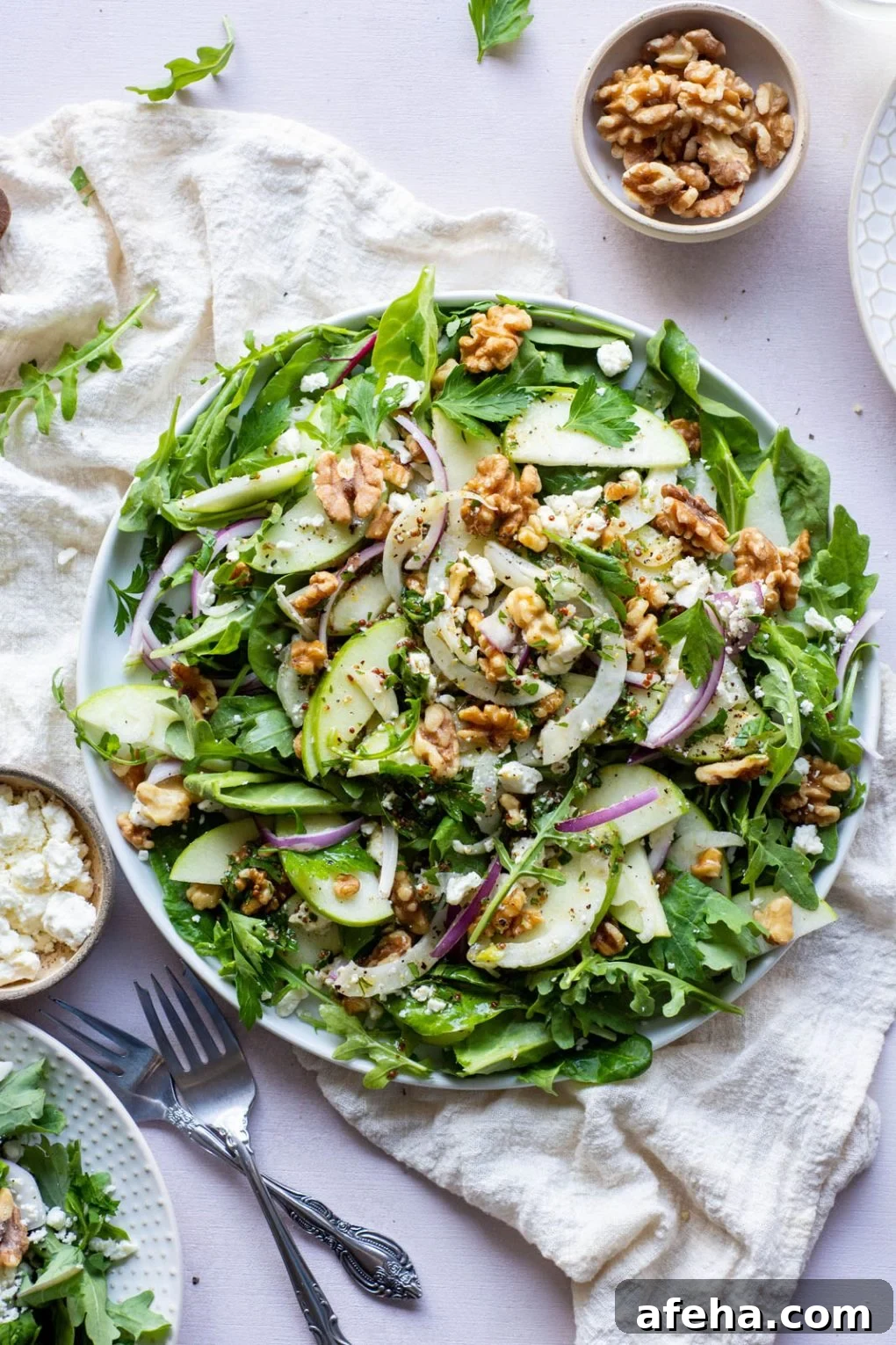 Large green salad on a round plate and a light colored background. Salad greens layered with thinly sliced green onion, thinly shaved fresh fennel, sliced red onion, walnuts, and torn parsley leaves. Drizzled with a mustardy dressing.