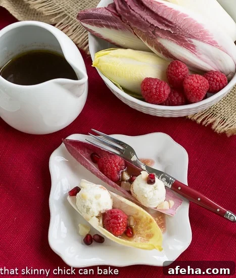 Endive Cups with Blue Cheese, Raspberries and Macadamia Nuts on a square white plate with a drizzle of vinaigrette.