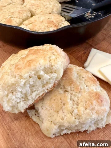 Baked homemade biscuits on a cutting board with a cast iron skillet and butter.