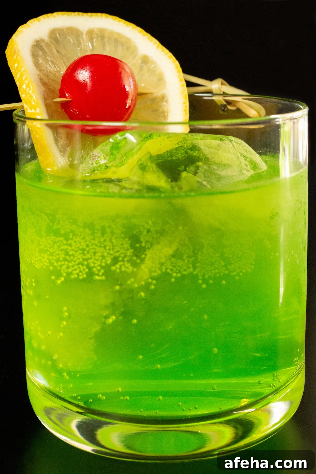 A lowball glass is filled with a neon green Midori Sour cocktail that is garnished with a lemon wheel and maraschino cherry.