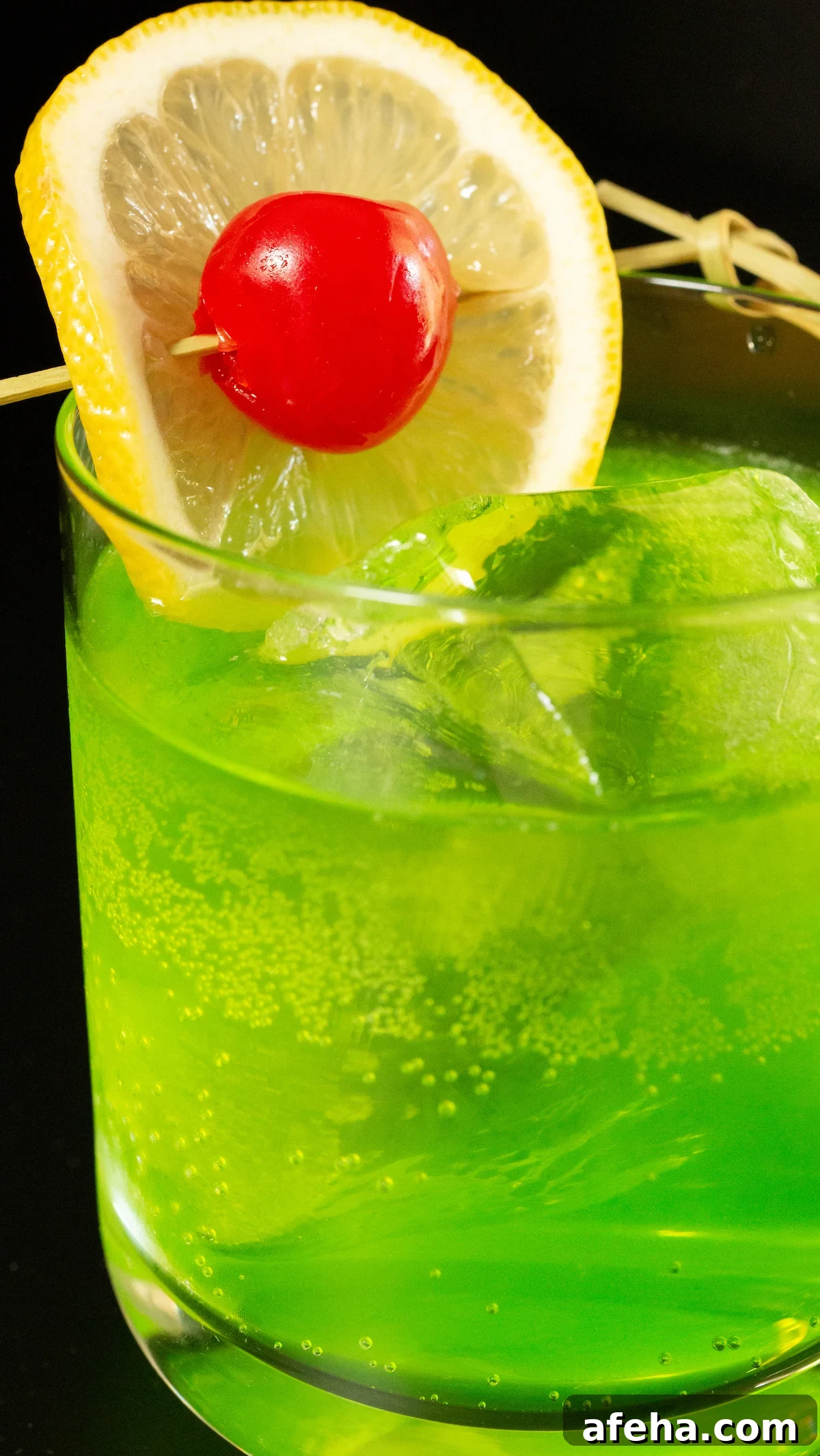 A lowball glass with a large block of ice is filled with a bright neon green Midori Sour cocktail that's garnished with a lime wheel and a maraschino cherry on a skewer.