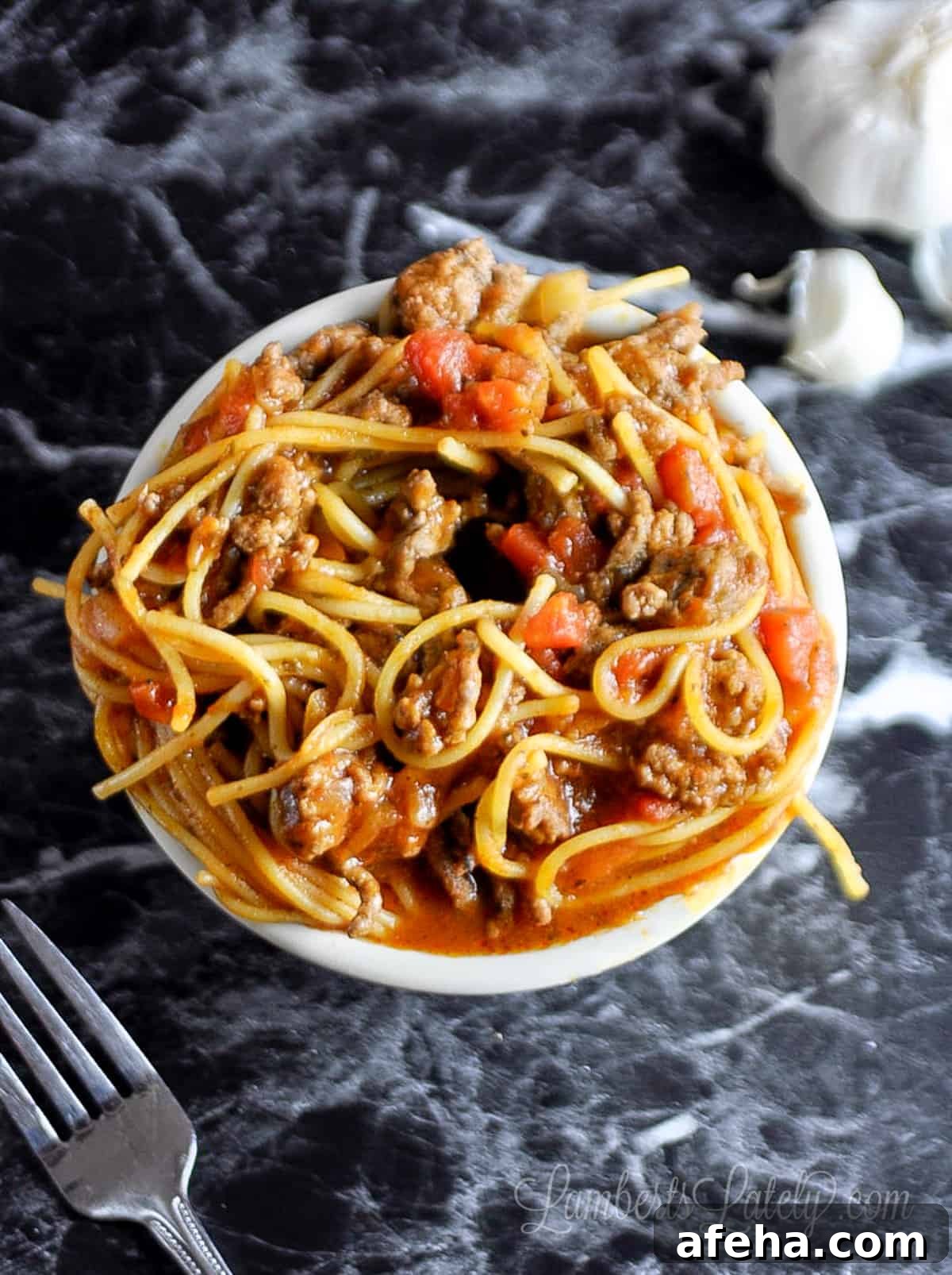looking down on a bowl of spaghetti on a dark countertop.