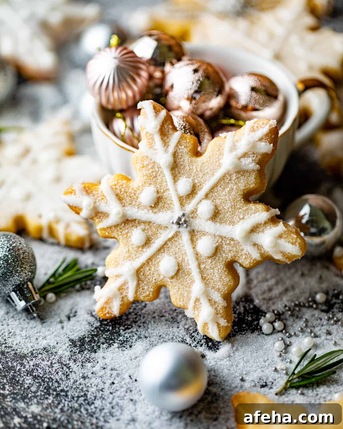a snowflake cookie standing up on a table with christmas bulbs around the cookie.