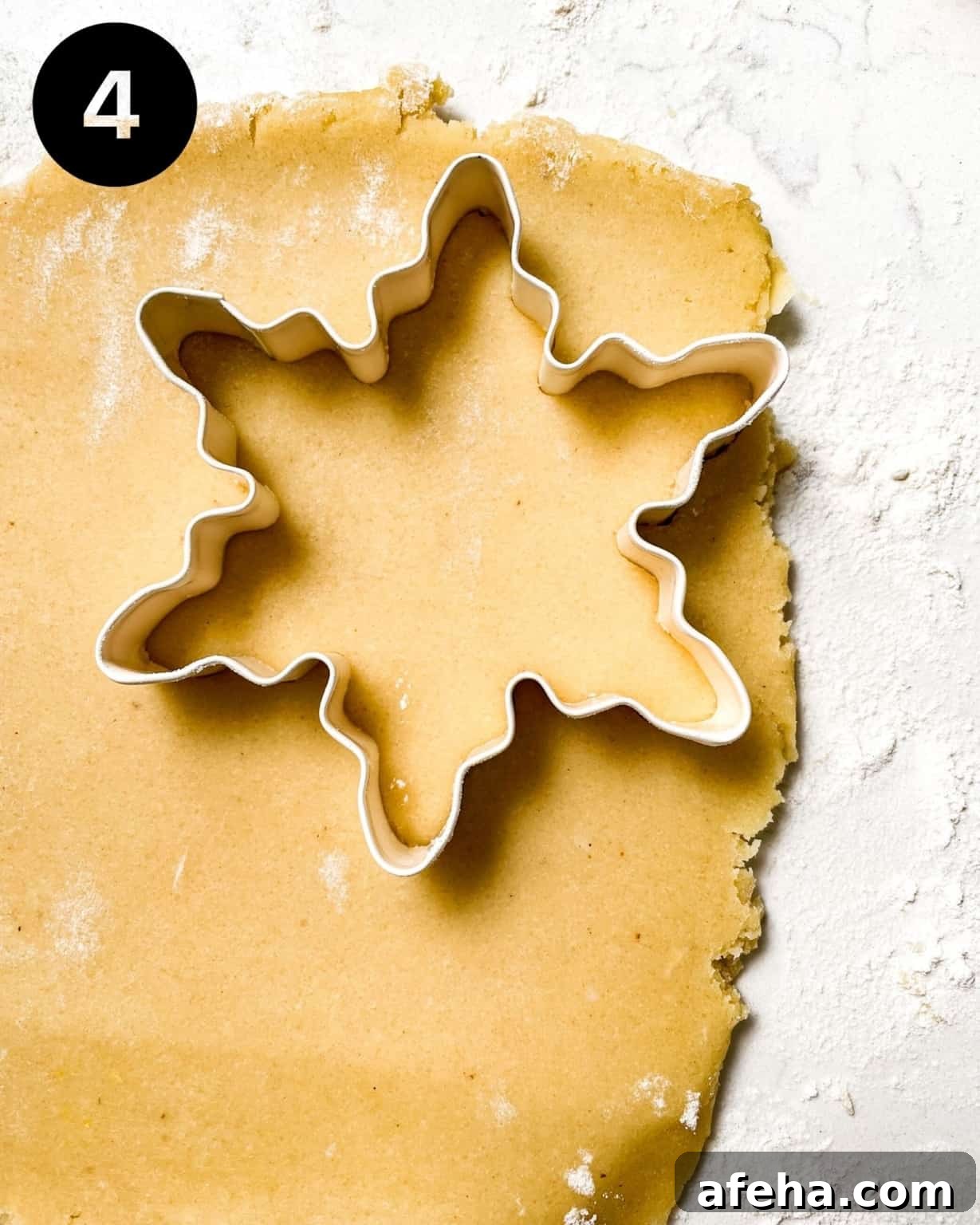 cookie dough rolled out onto a surface with a snowflake cookie cutter pressed into the dough.