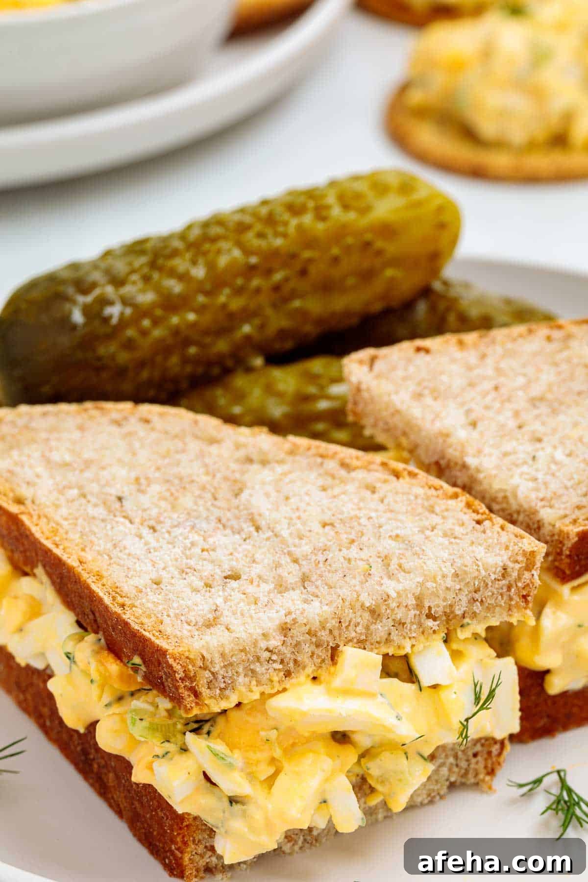 Dill pickle egg salad sandwich made with soft sliced bread filled with creamy egg salad, served with whole pickles on the side.