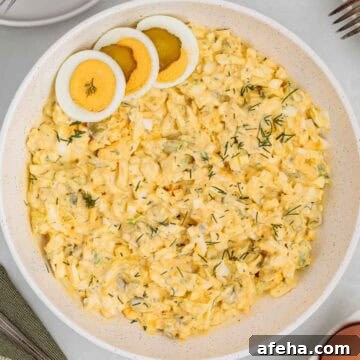 Close up of dill pickle egg salad in a serving bowl topped with sliced hard boiled eggs and sprinkled with fresh dill.