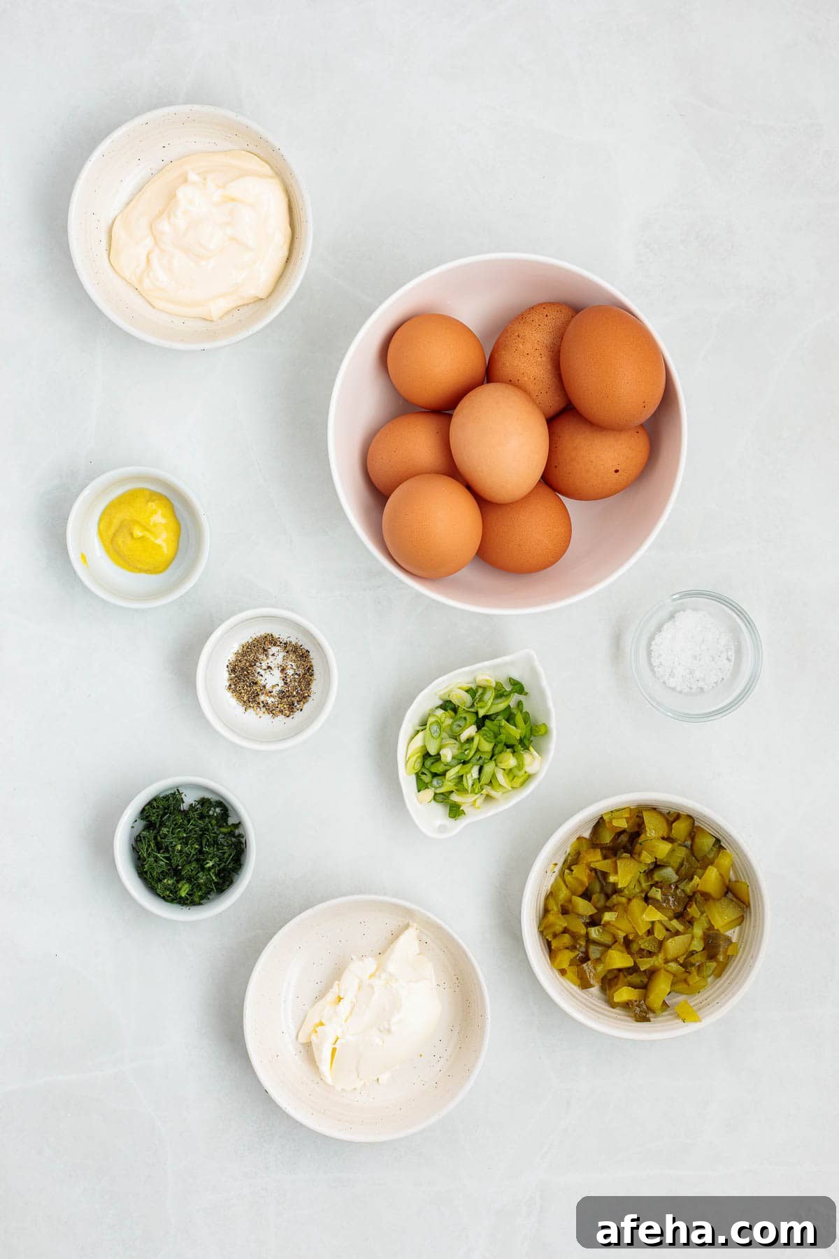 Ingredients for dill pickle egg salad arranged on a countertop including whole eggs, mayonnaise, cream cheese, mustard, chopped pickles, green onions, dill, salt, and pepper.