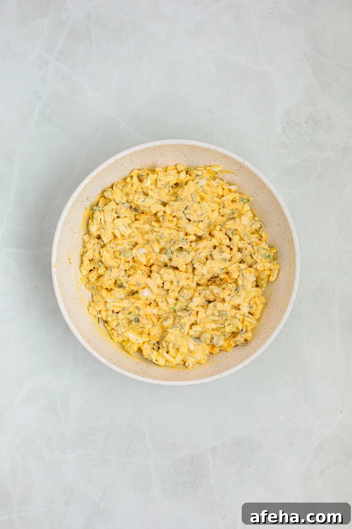 Finished dill pickle egg salad in a bowl with chopped eggs, pickles, and fresh dill fully mixed into a creamy texture.