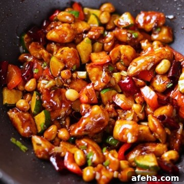 Kung pao chicken coated in a glossy sauce with veggies, peanuts, and dried red chilies.