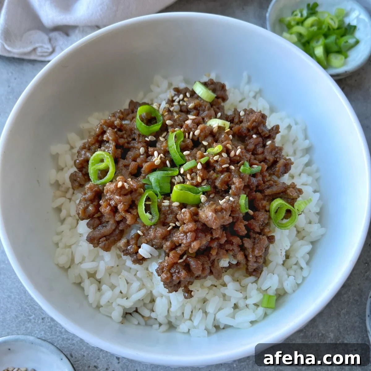 Mongolian Beef with Ground Beef: Quick Savory Stir-Fry Recipe 2 A bowl of white rice topped with savory Mongolian Ground Beef, sliced green onions, and sesame seeds.