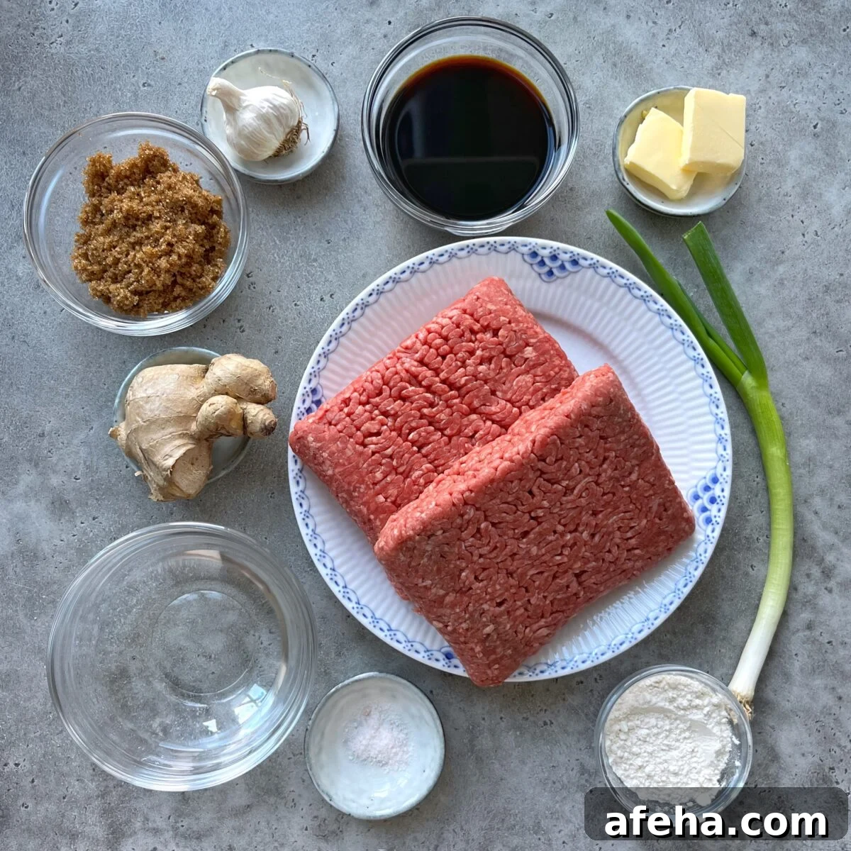 Mongolian Beef with Ground Beef: Quick Savory Stir-Fry Recipe 4 Ingredients for a recipe arranged on a gray surface, including ground beef, garlic, ginger, brown sugar, soy sauce, butter, green onion, flour, salt, and a small bowl of water.