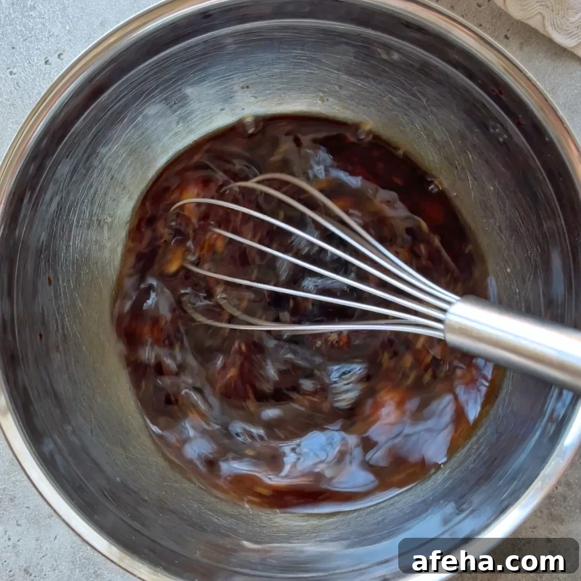 Mongolian Beef with Ground Beef: Quick Savory Stir-Fry Recipe 6 A metal whisk stirs a dark Mongolian Ground Beef sauce in a stainless steel mixing bowl.