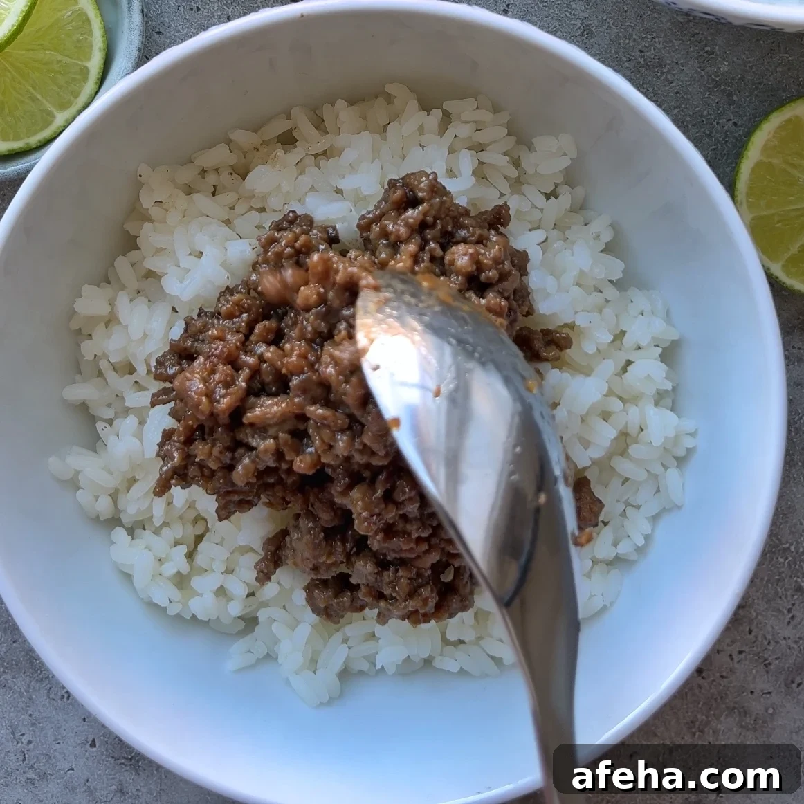 Mongolian Beef with Ground Beef: Quick Savory Stir-Fry Recipe 8 A spoon is serving Mongolian Ground Beef onto a bowl of white rice, with lime slices visible on the side.