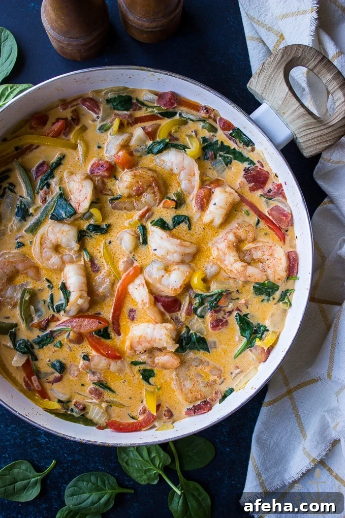 Overhead photo of Cajun Shrimp Linguine in skillet with a white and yellow check dish cloth and a wooden salt and pepper shaker.
