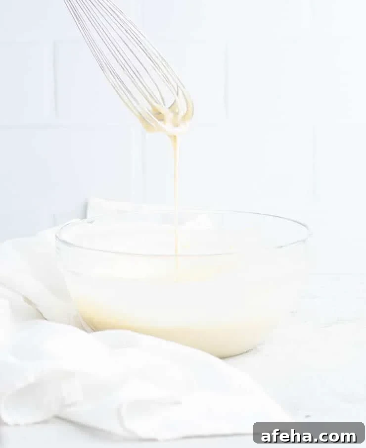Rosette batter dripping off a whisk and into a clear bowl.
