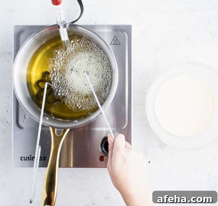 Overhead view of a batter-laden rosette iron in a small pot of hot oil frying.
