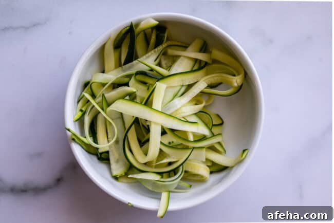 zucchini ribbons in a white bowl, made from a vegetable peeler.