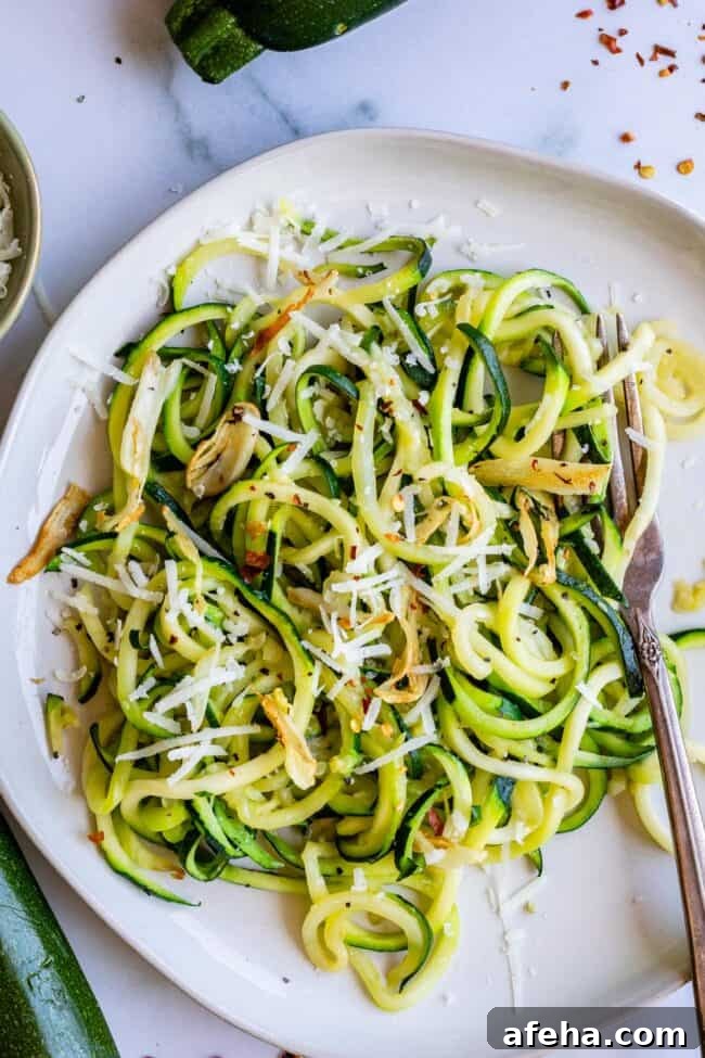 zucchini noodles on a white plate with cheese and spices, overhead.