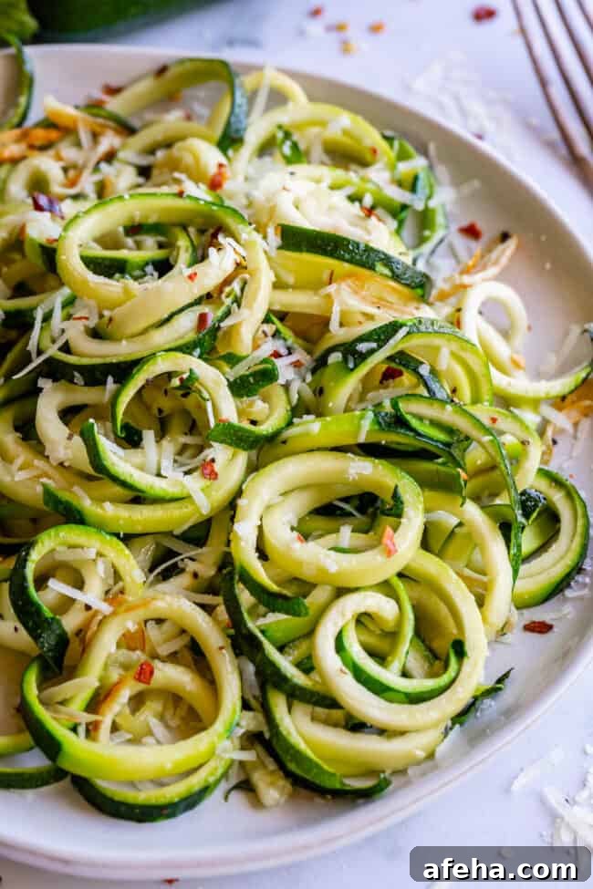 curly zoodles with parmesan and red pepper flakes on a white plate.