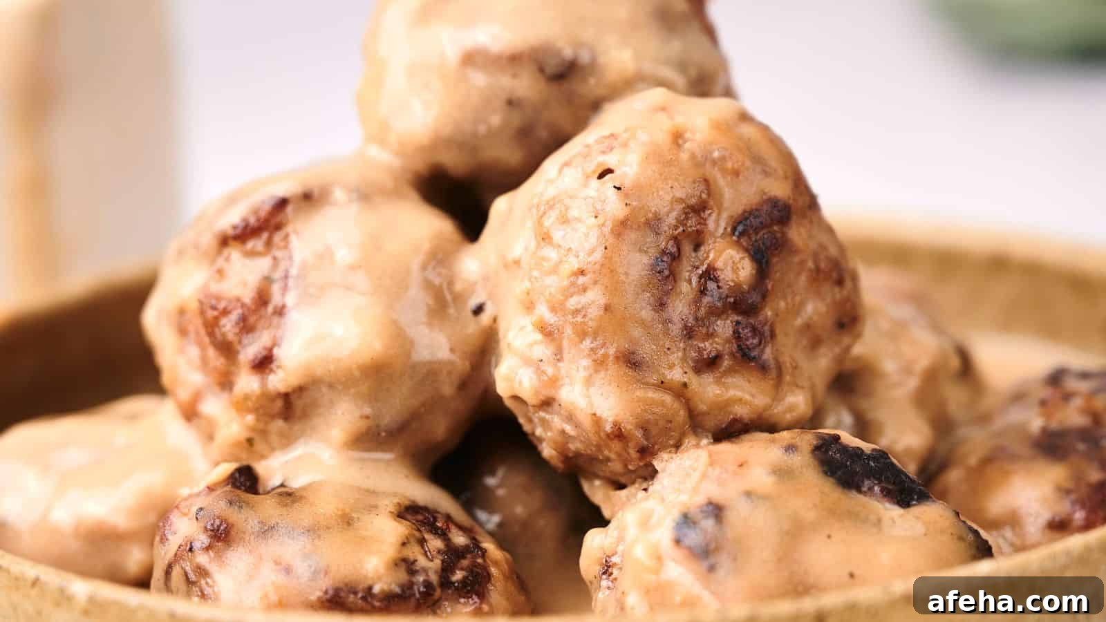 A close-up of Swedish meatballs covered in a creamy sauce, piled in a wooden bowl.