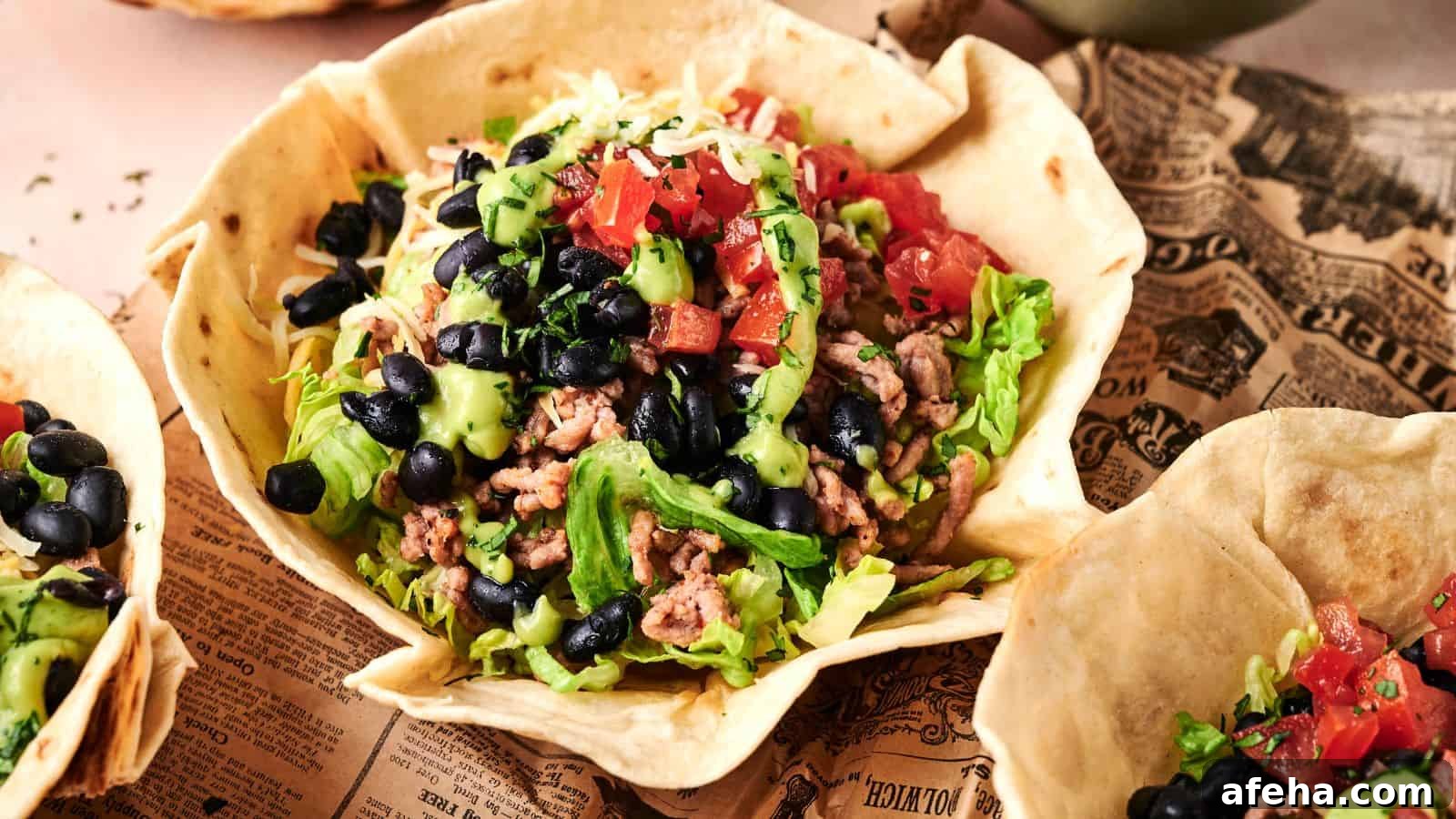A taco salad served in an edible tortilla bowl, topped with ground meat, lettuce, black beans, diced tomatoes, avocado, and shredded cheese.