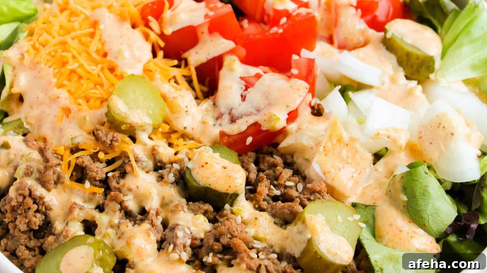 Close-up of a salad featuring ground beef, sliced pickles, diced tomatoes, shredded cheese, and diced onions, topped with a creamy dressing.