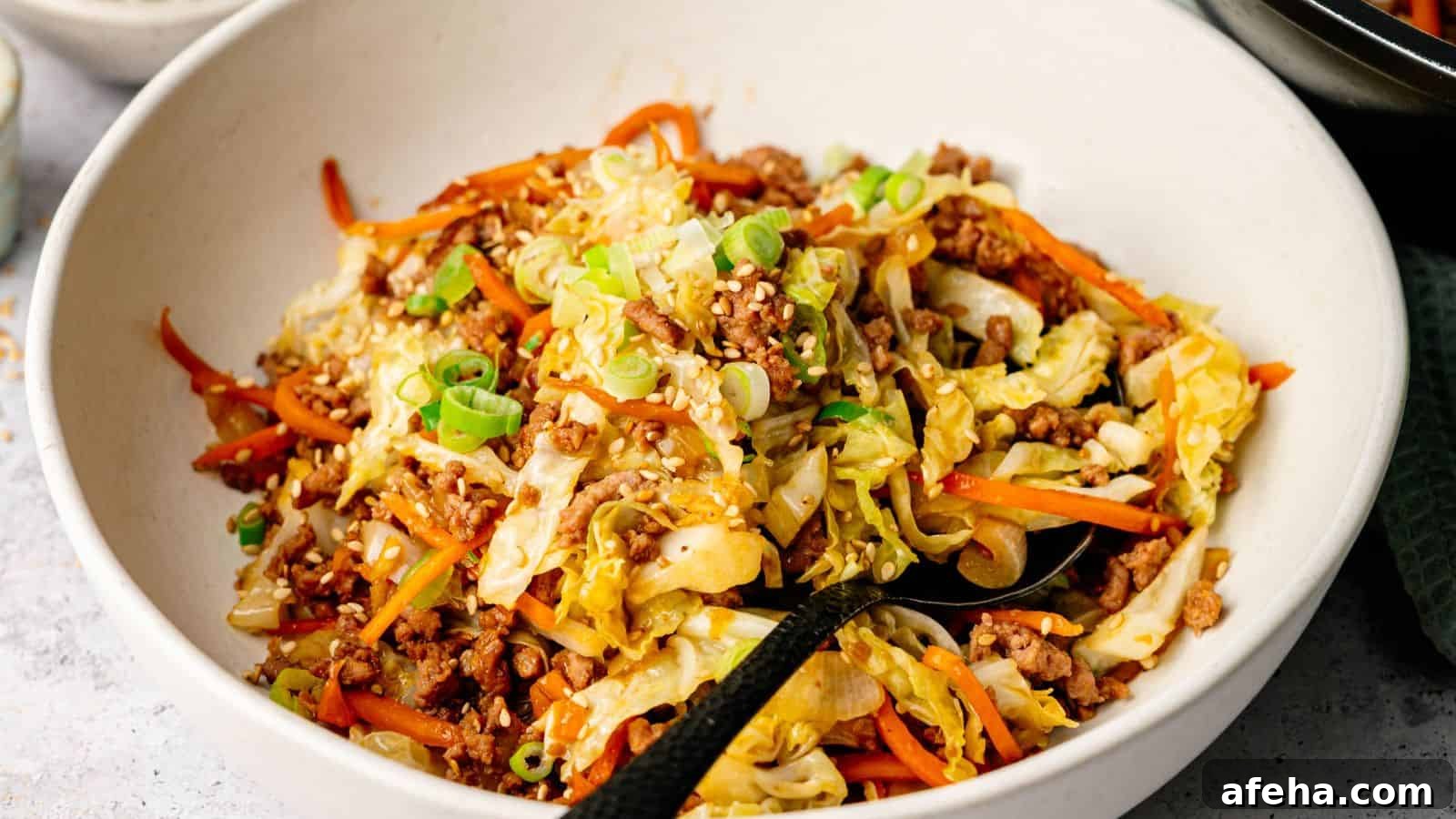 A bowl of stir-fried ground meat, shredded cabbage, and carrots, topped with sesame seeds and chopped green onions.