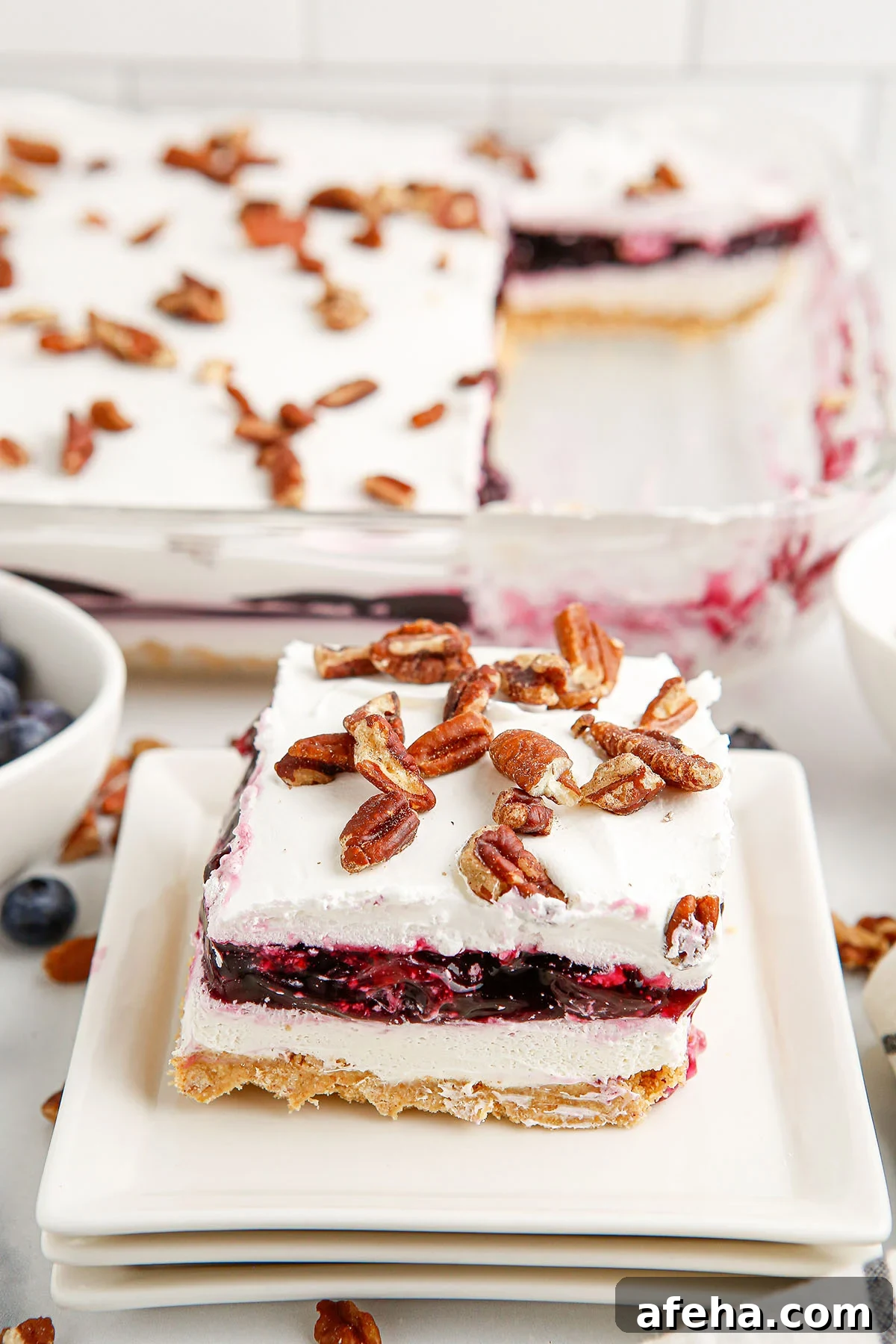 A slice of Blueberry Delight on a white plate topped with chopped pecans.