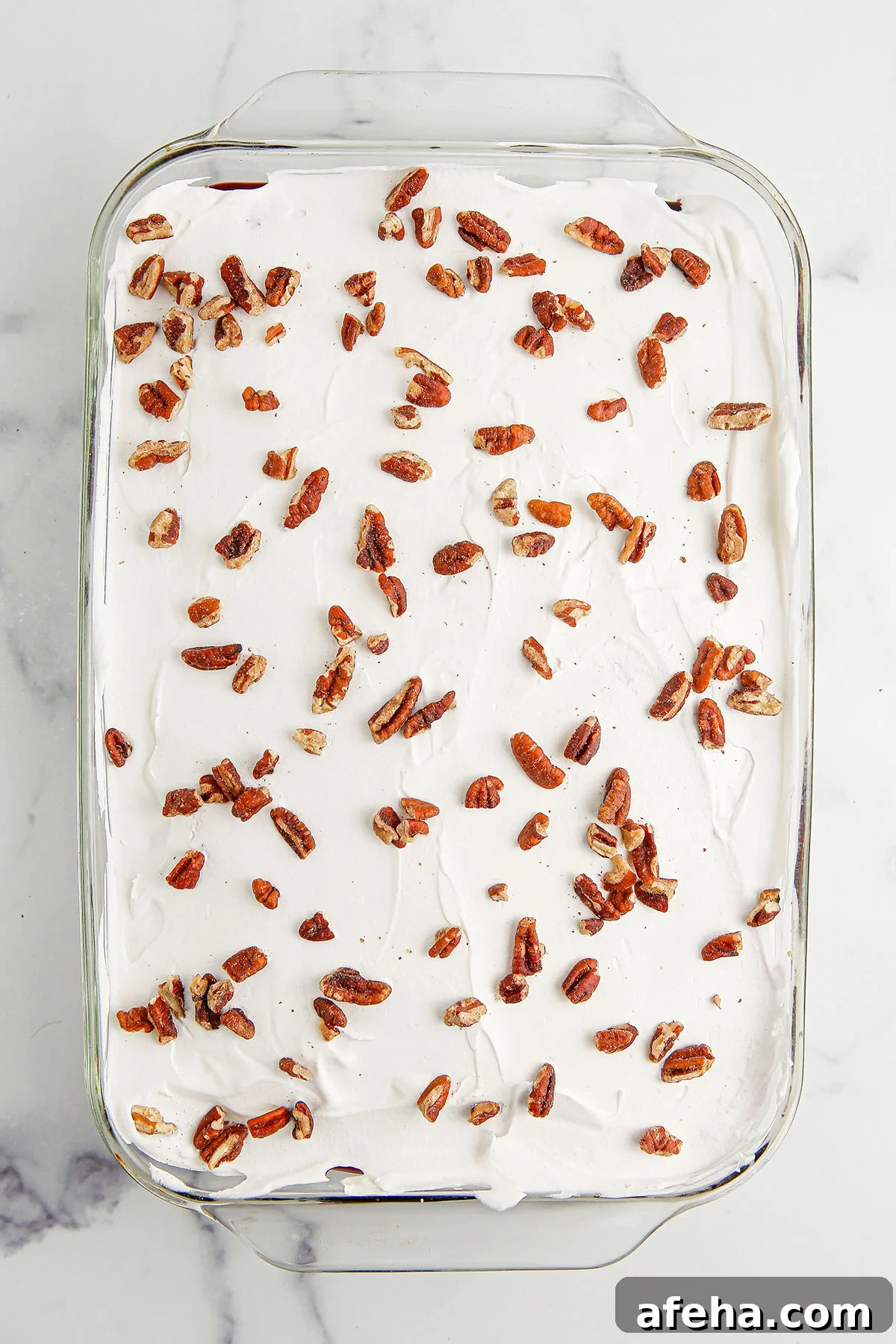 Chopped pecans sprinkled over the whipped topping layer in the glass dish.