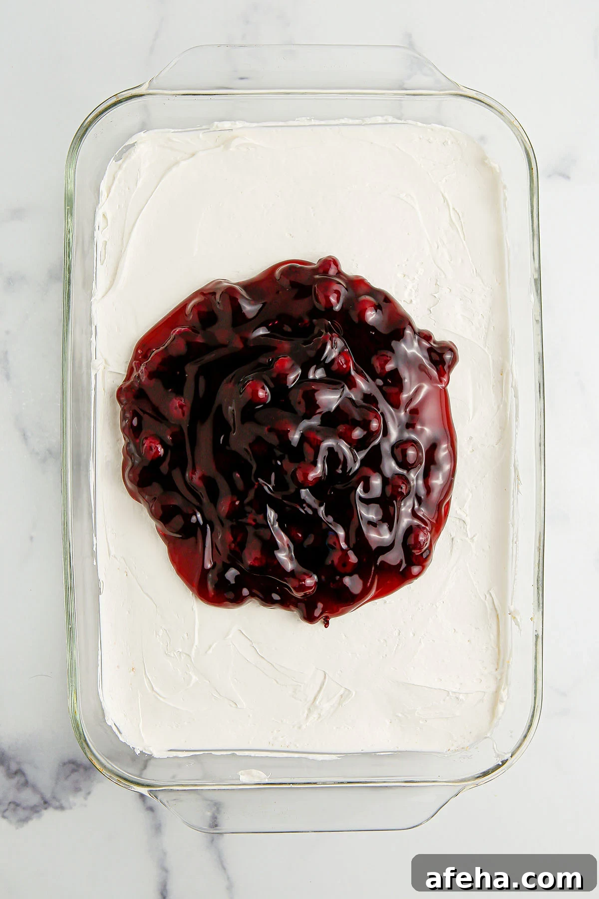 Blueberry pie filling poured over the cheesecake layer in glass dish.