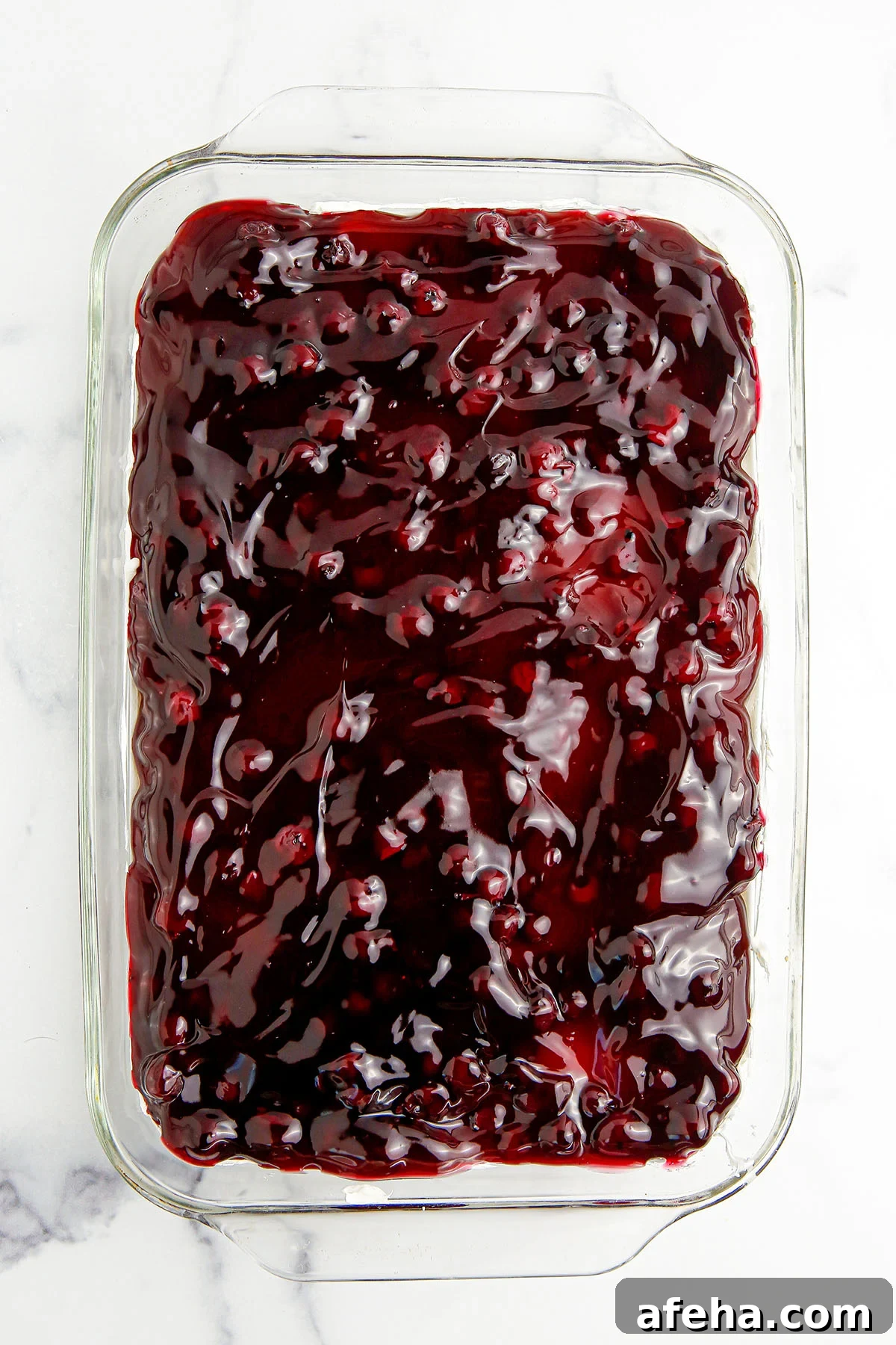 Blueberry pie filling spread over the cheesecake layer in glass dish.