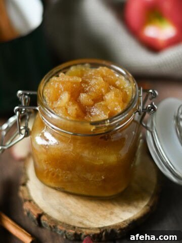 Applesauce in a clear jar with cinnamon sticks next to it.