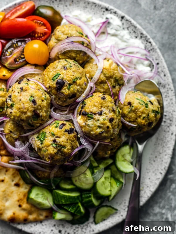 Savory Ground Chicken Meatballs with Tangy Tomato Sauce 11 Close up of meatballs on a serving platter with tzatziki, fresh veggies, and pita.