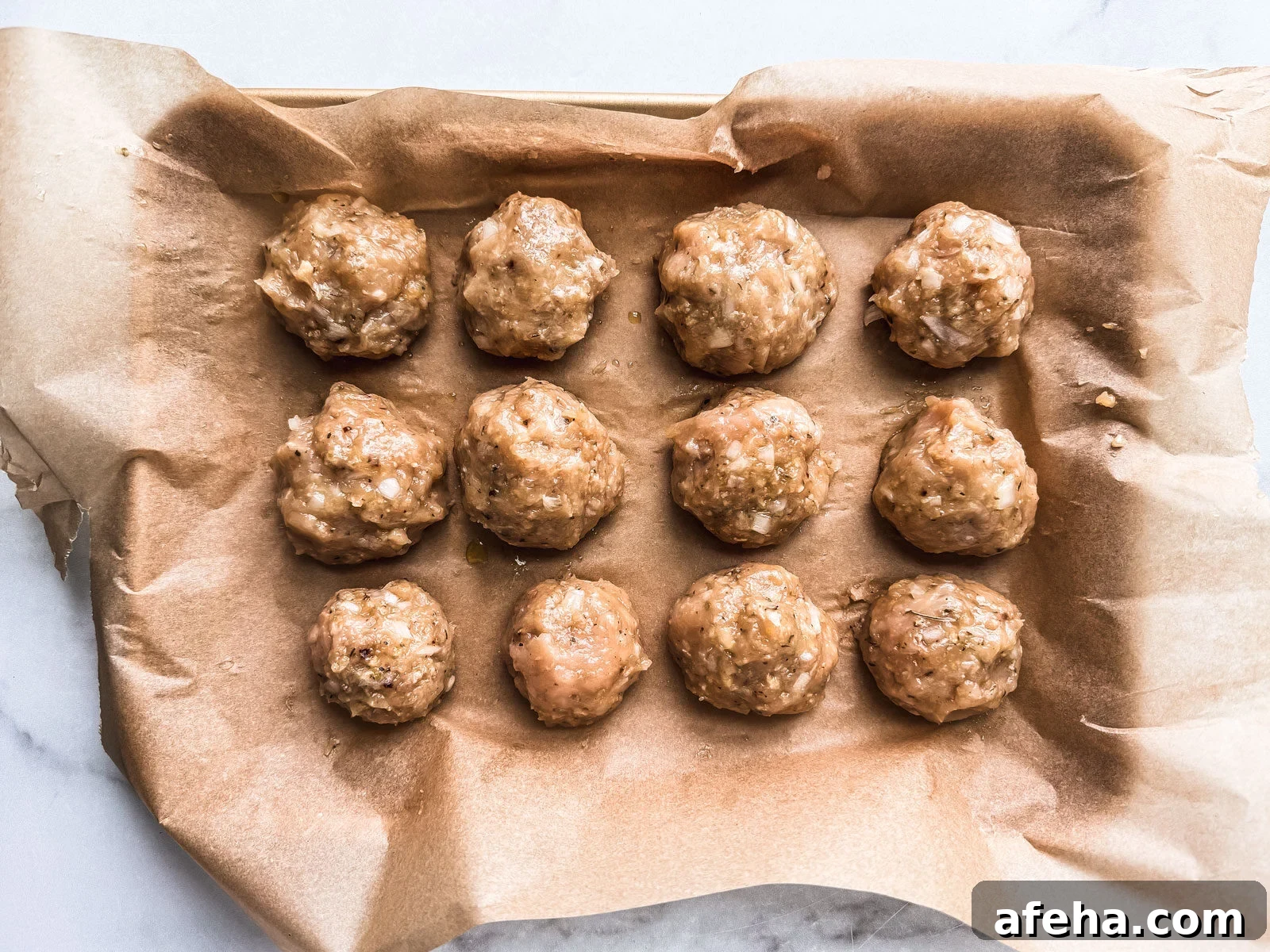 Savory Ground Chicken Meatballs with Tangy Tomato Sauce 4 Uncooked chicken meatballs on a baking sheet.