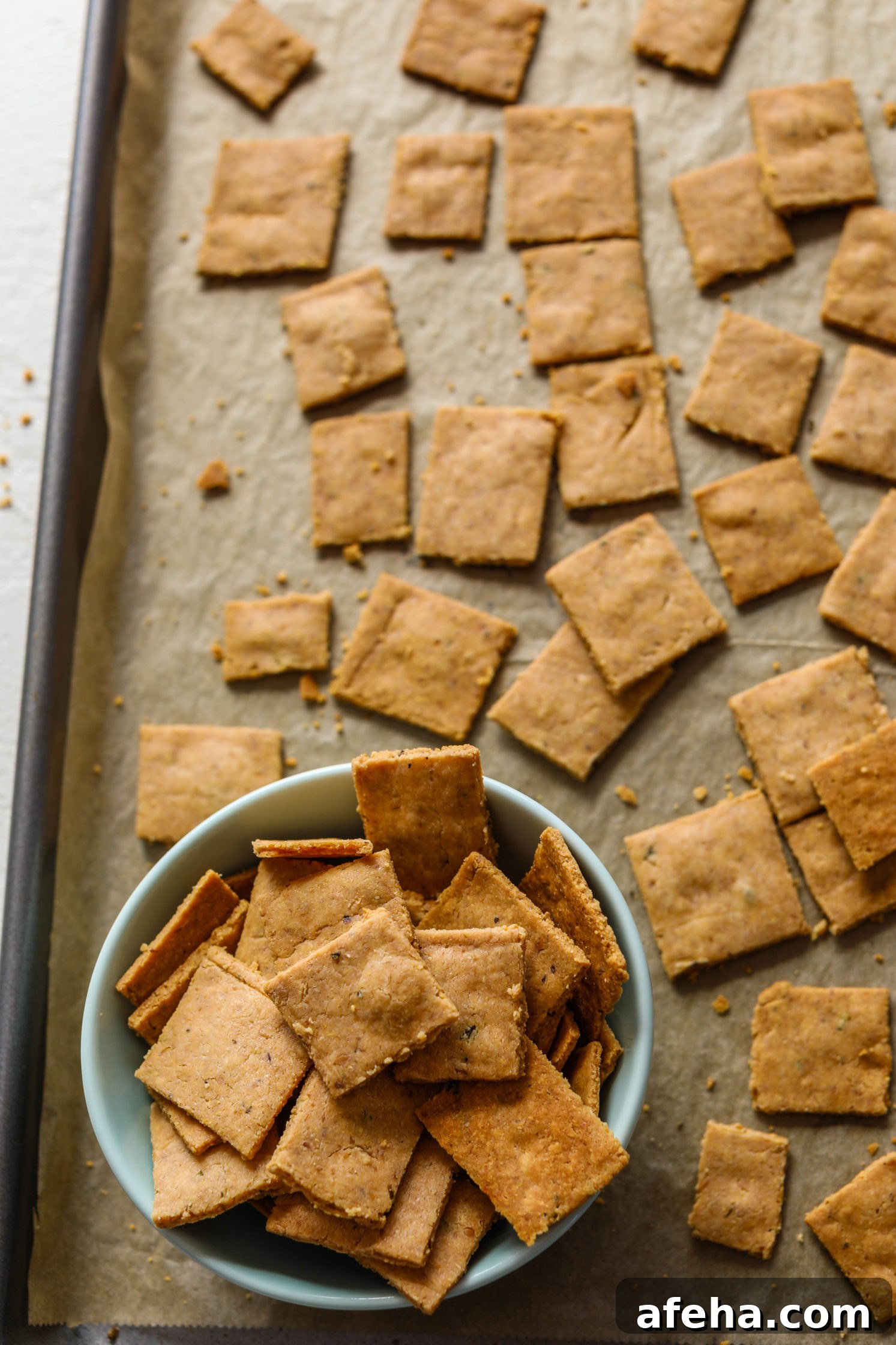 Grain-Free Almond Flour Crackers on parchment lined baking sheet with bowl of crackers on bottom