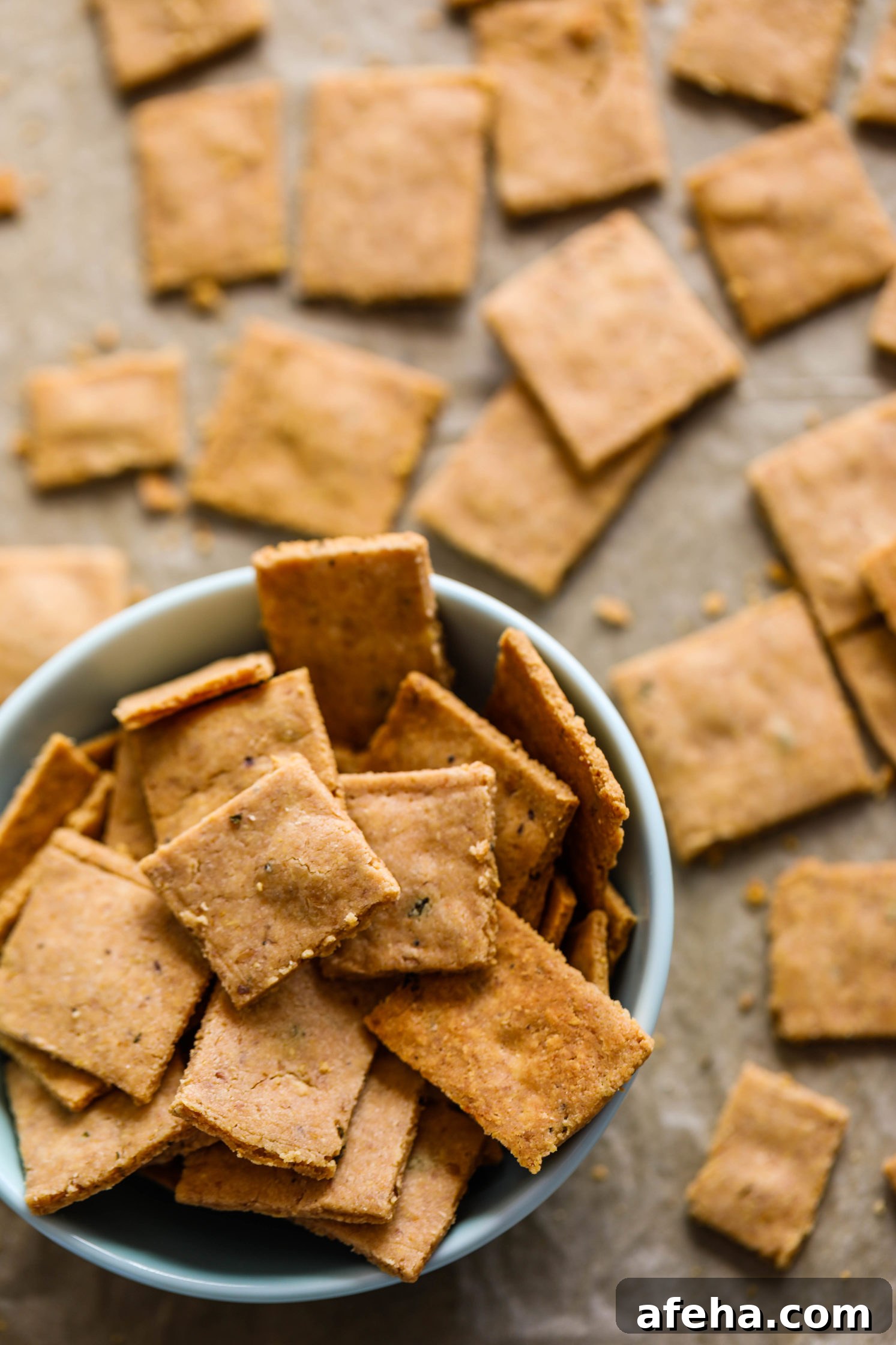 Grain-Free Almond Flour Crackers on parchment lined baking sheet with bowl of crackers on bottom