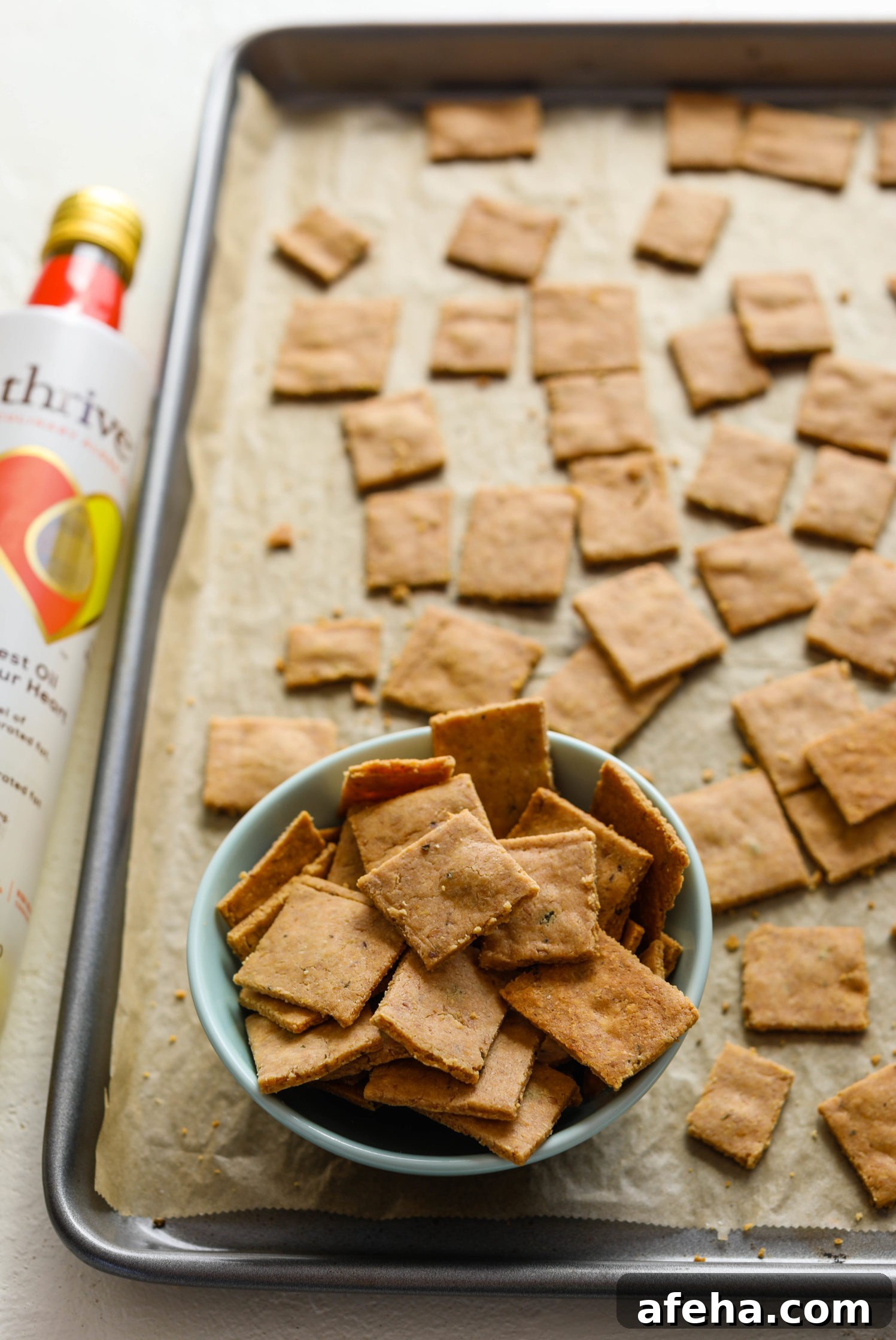 Grain-Free Almond Flour Crackers on parchment lined baking sheet with bowl of crackers on bottom