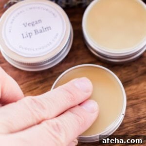 Dabbing two fingers into a vegan lip balm tin.