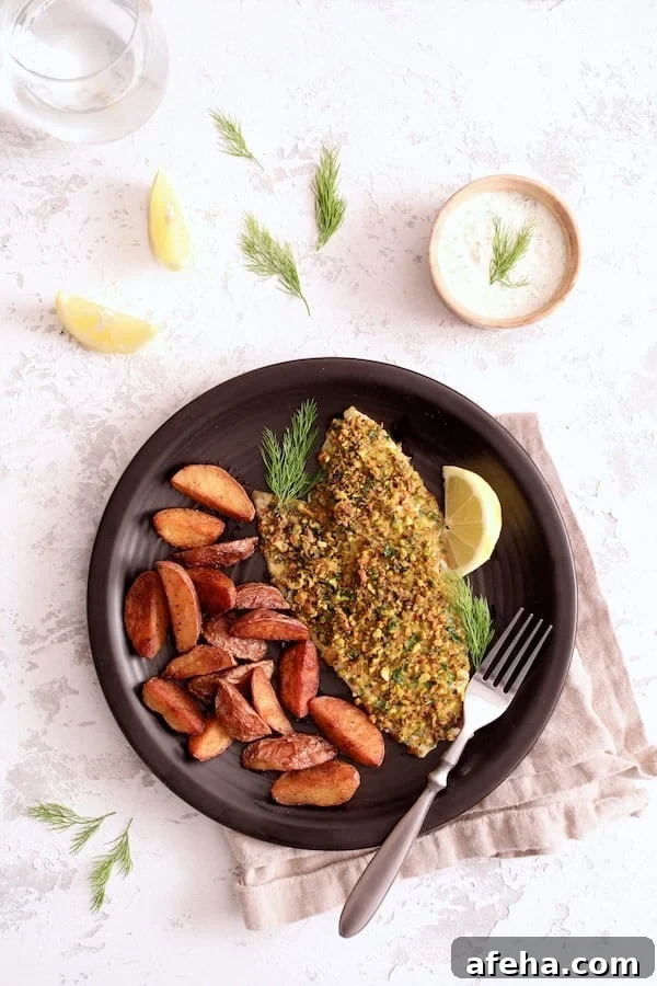 Pistachio-Crusted Fish with Lemon-Dill Aioli 5 Photo of Pistachio-Crusted Fish with Lemon-Dill Aioli served with roasted potatoes garnished with lemon slices and dill sprigs on black plate.