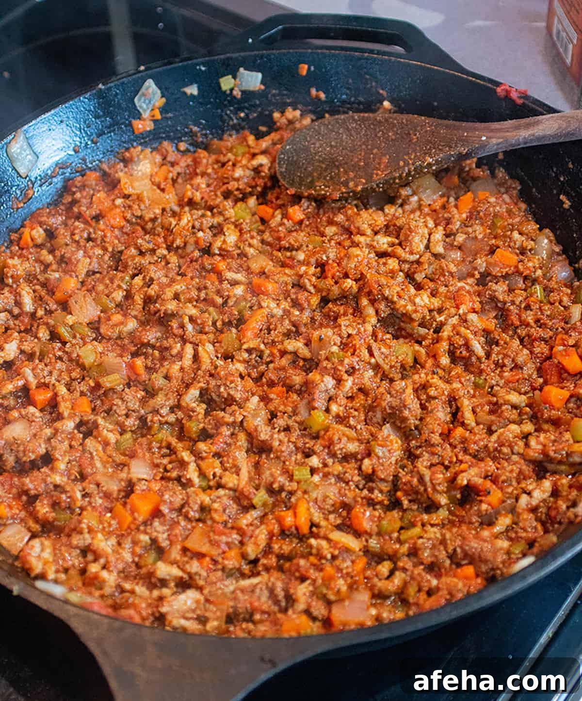 Ground meat and sausage being cooked in a large cast iron skillet.