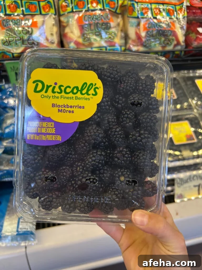 a hand holding a carton of blackberries in the Trader Joe's produce aisle