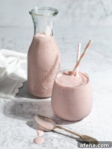 A glass and a carafe of strawberry lassi on a white background.